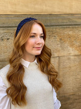 Load image into Gallery viewer, Navy ruffled headband worn over long auburn waves, shown in three-quarter view against a stone wall.
